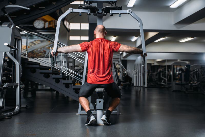 Atleta muscolare sulla macchina di esercizio, vista posteriore fotografia stock Atleta muscolare sulla macchina di esercizio, vista posteriore fotografia stock