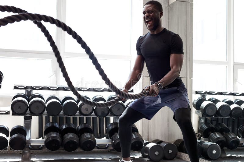 Atleta negro haciendo ejercicio de cuerda de batalla en el gimnasio de ballesta