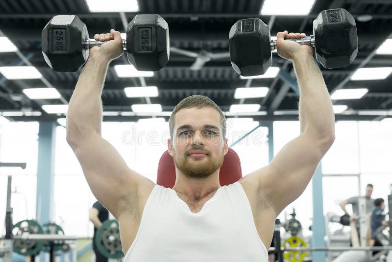 Atleta que faz o exercício para ombros com os pesos que sentam-se em um banco Trens musculares novos do homem no gym fotos de stock Atleta que faz o exercício para ombros com os pesos que sentam-se em um banco Trens musculares novos do homem no gym fotos de stock