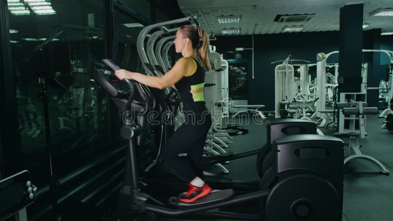 Atletische vrouw die oefent op een elliptische machine. opleiding van spier - en vrouwenbeweging in de moderne sportschool. in een