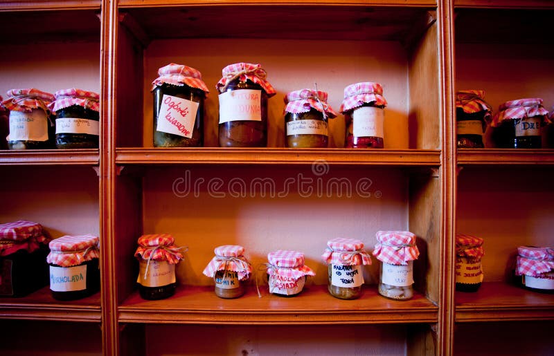 Home made preserves in red and white covered jars on wooden shelves in kitchen. Home made preserves in red and white covered jars on wooden shelves in kitchen