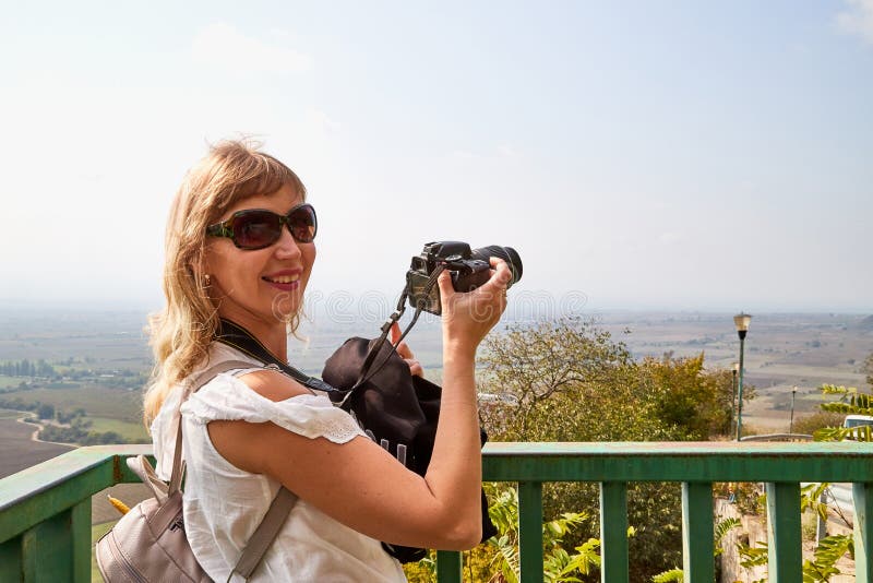 Atractiva y hermosa joven que es mujer viajera fotógrafa sosteniendo una moderna cámara espejo en las manos al aire libre imagen de archivo