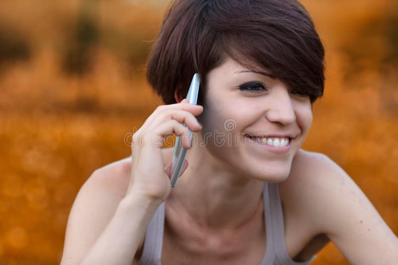 Attractive woman chatting on her mobile phone outdoors in a close up on her hand and focus to her eye and happy smile. Attractive woman chatting on her mobile phone outdoors in a close up on her hand and focus to her eye and happy smile