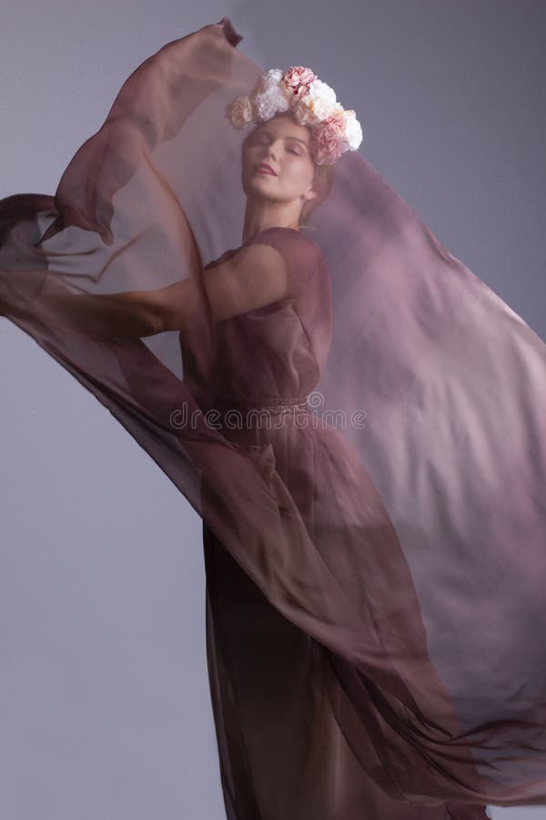 Atrakcyjna młoda kobieta tańczy, mając na sobie sukienkę z chiffonem i szal i kwiatową sukienkę z głowy.