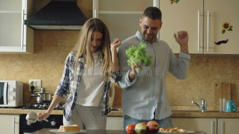 Atrakcyjna młoda radosna para zabawa śpiew i tana w kuchni podczas gdy gotujący w domu