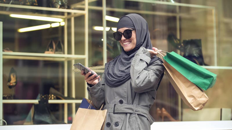 Atrakcyjna uśmiechnięta kobieta w hijab zakupy i gawędzenie na telefonie z przyjacielem obraz royalty free Atrakcyjna uśmiechnięta kobieta w hijab zakupy i gawędzenie na telefonie z przyjacielem obraz royalty free