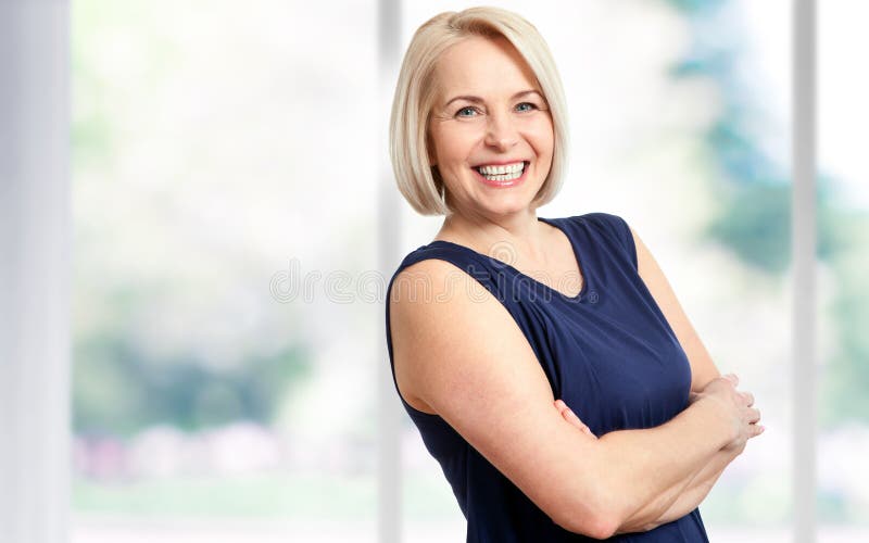Atrakcyjna w średnim wieku kobieta z pięknym uśmiechem blisko okno fotografia royalty free