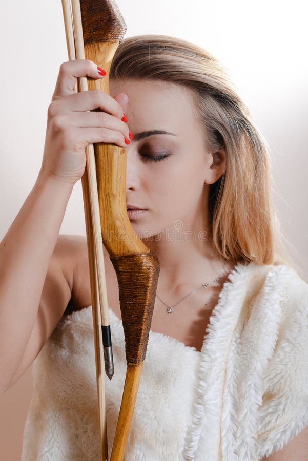 Atrakcyjnej czułej szczerej blond młodej kobiety dziewczyny mienia łęku i strzała piękni oczy zamykali być ubranym kaross lub bia obraz stock Atrakcyjnej czułej szczerej blond młodej kobiety dziewczyny mienia łęku i strzała piękni oczy zamykali być ubranym kaross lub bia obraz stock