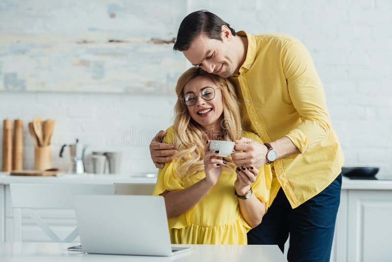 Att bry sig mannen som ger kaffe till att le kvinnaarbete. Att bry sig mannen som ger kaffe till att le kvinnan som arbetar vid bärbara datorn