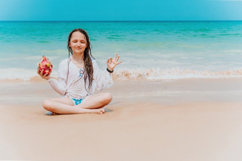 Att charma tonåring i en vit skjorta och med långa hårmeditat i ett lotus läge på kusten I händerna på en drake arkivbilder Att charma tonåring i en vit skjorta och med långa hårmeditat i ett lotus läge på kusten I händerna på en drake arkivbilder