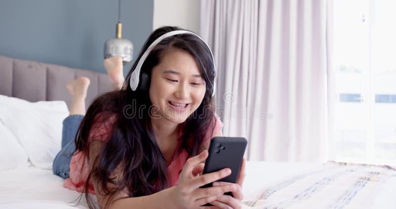Att lyssna på musik på hörlurar kvinnor som leker och använder smartphone på sängen lager videofilmer
