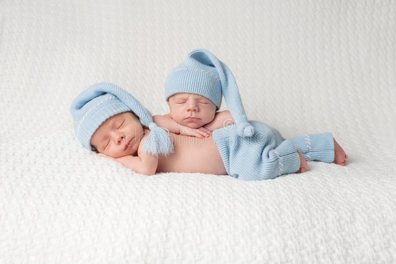 One month old fraternal, twin baby boys wearing light blue stocking caps and sleeping on a white blanket. One month old fraternal, twin baby boys wearing light blue stocking caps and sleeping on a white blanket.