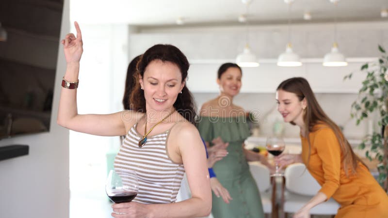 Attention jeune femme en robe orange tenant un verre de vin et dansant avec des amies lors d'une fête animée banque de vidéos