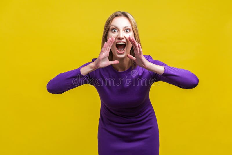 Attention! Portrait of aggressive woman in elegant purple dress holding her hands near wide open mouth and shouting announcement, crazy furious face. indoor studio shot isolated on yellow background. Attention! Portrait of aggressive woman in elegant purple dress holding her hands near wide open mouth and shouting announcement, crazy furious face. indoor studio shot isolated on yellow background