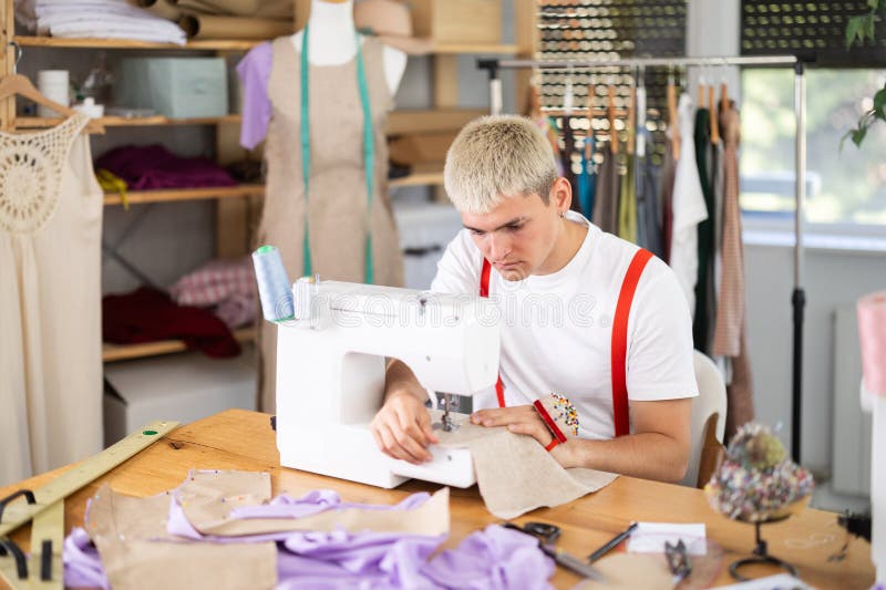 Attentive man tailor sewing textile using sewing machine sitting at workplace in fashionable sewing atelier stock image