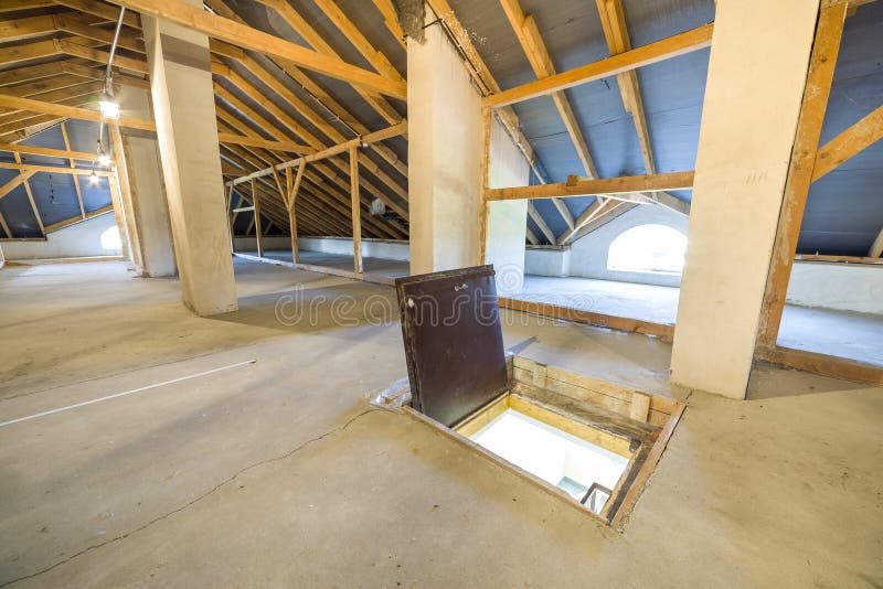 Attic of a building with wooden beams of a roof structure and a fire exit door in floor.