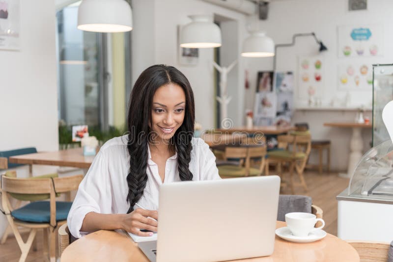 Attractive african american smiling businesswoman working on laptop while sitting at cafe royalty free stock image Attractive african american smiling businesswoman working on laptop while sitting at cafe royalty free stock image