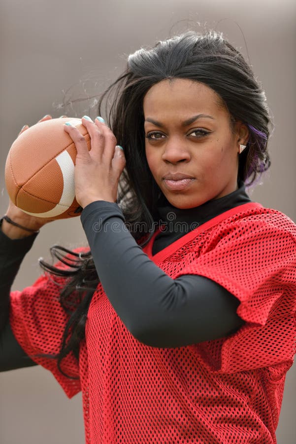 Attractive young African American woman in red practice mesh jersey holding a generic American Football - ready to throw. Attractive young African American woman in red practice mesh jersey holding a generic American Football - ready to throw