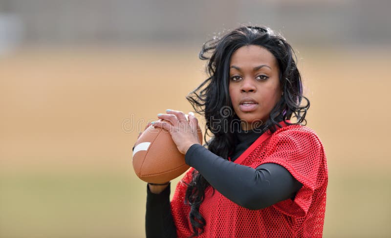 Attractive young African American woman in red practice mesh jersey holding a generic American Football - ready to throw. Attractive young African American woman in red practice mesh jersey holding a generic American Football - ready to throw