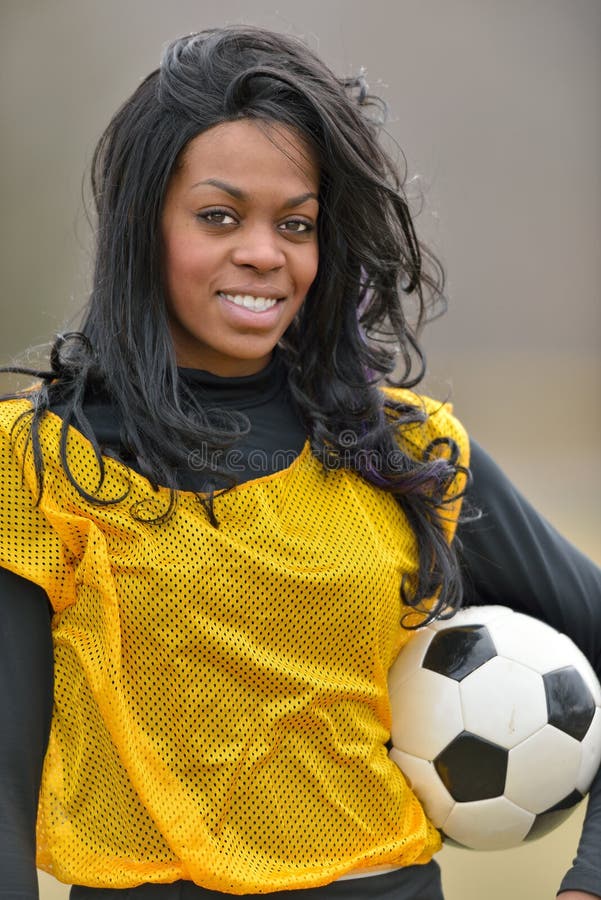 Attractive young African American woman in yellow practice mesh jersey holding a generic soccer ball. Attractive young African American woman in yellow practice mesh jersey holding a generic soccer ball