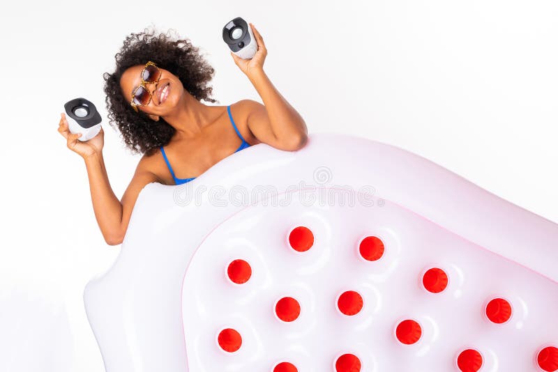 Attractive african girl in a blue bathing suit and glasses holds a swimming mattress and holds speakers for music