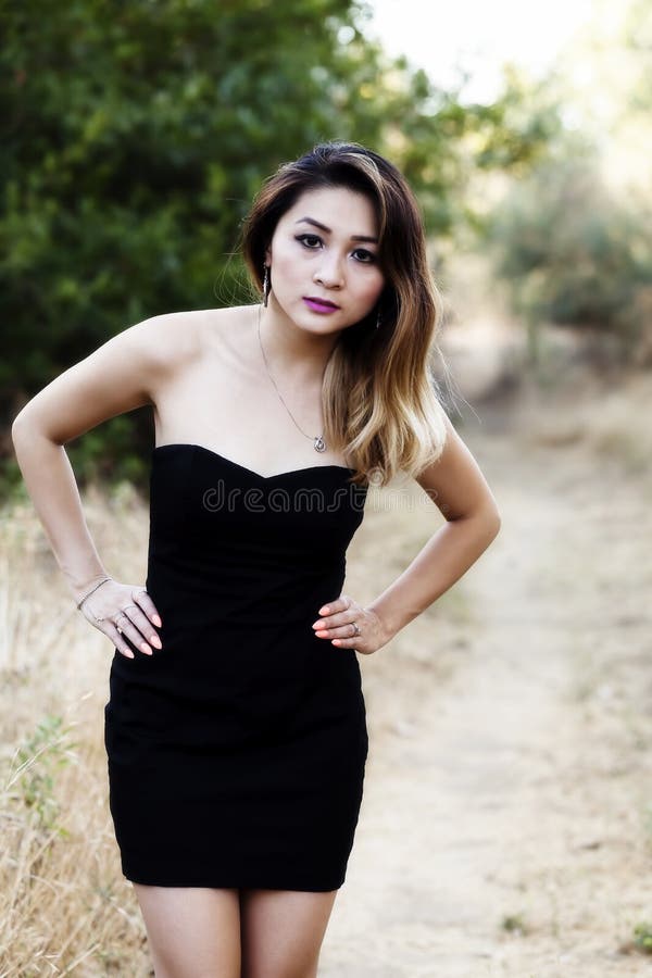 Attractive Asian American Woman Arms Akimbo Standing Outdoors In Black Dress. Attractive Asian American Woman Arms Akimbo Standing Outdoors In Black Dress