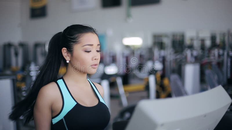 Attractive asian girl running on the treadmill in the gym. Right 3/4 face portrait