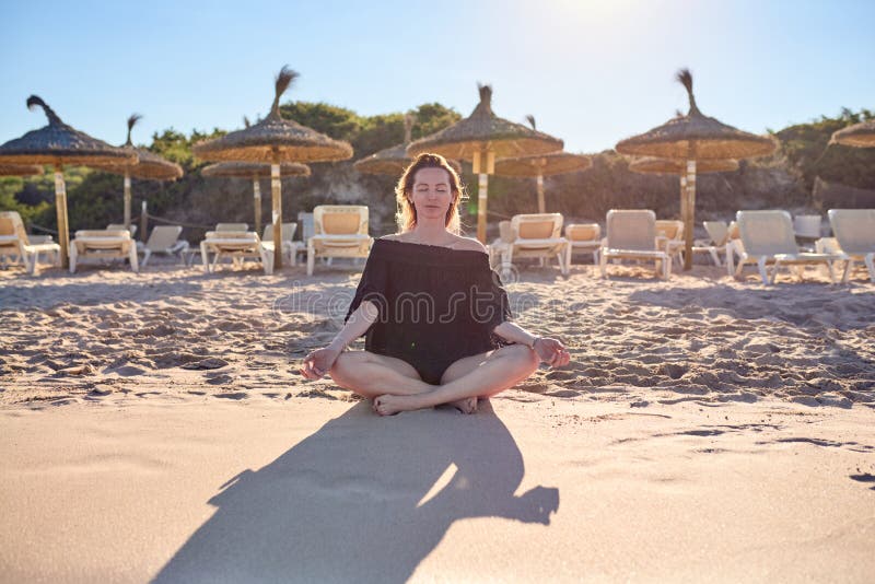 Attractive barefoot woman meditating at the beach