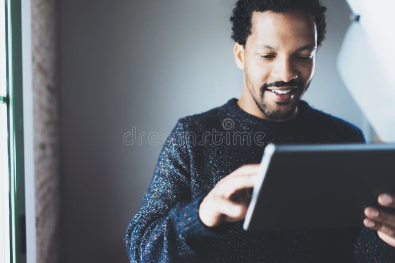 Attractive bearded African businessman using tablet while standing at his modern home office.Concept of young people