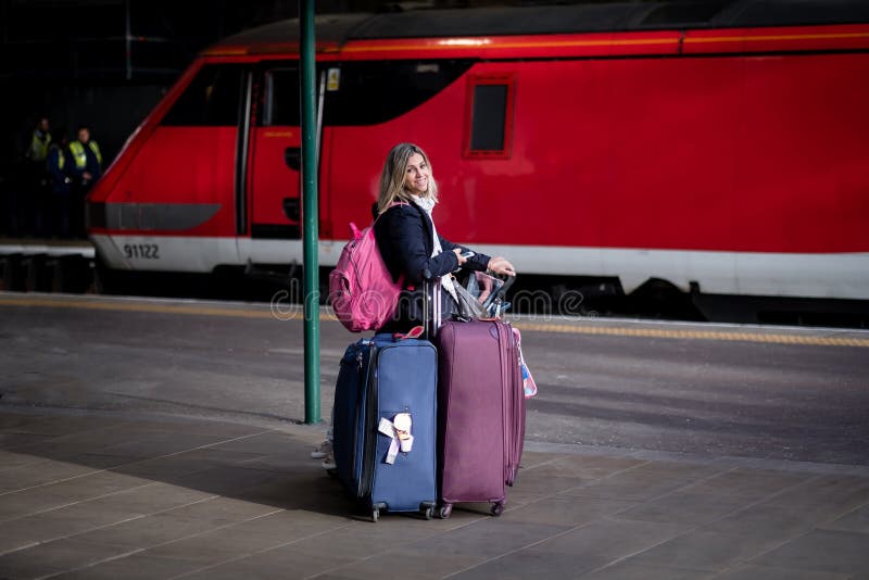 Attractive blond woman looking tired and busy with many bags and luggage at a train station with red train in the stock photos Attractive blond woman looking tired and busy with many bags and luggage at a train station with red train in the stock photos