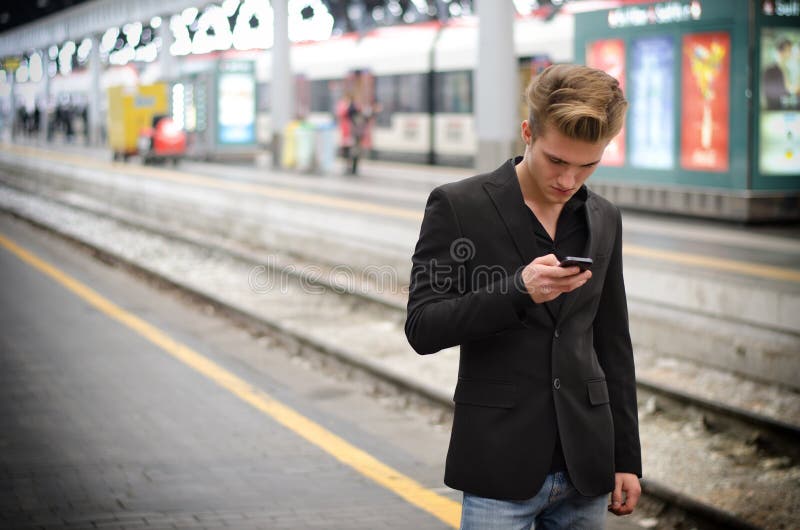 Attractive blond young man in station using cellphone