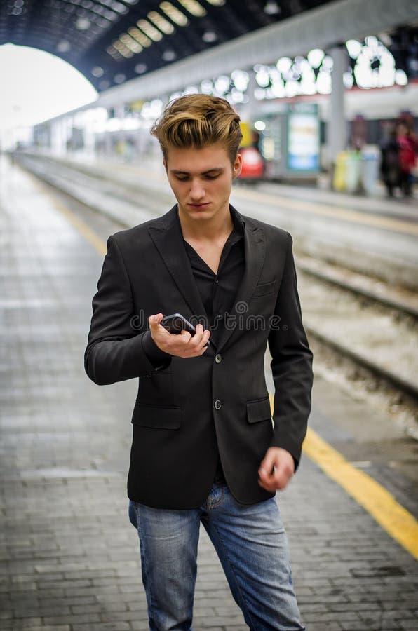 Attractive blond young man in station using cellphone