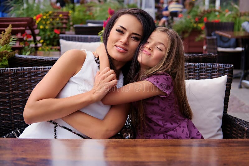 A woman hugs cute little girl at the table in an open air cafe.