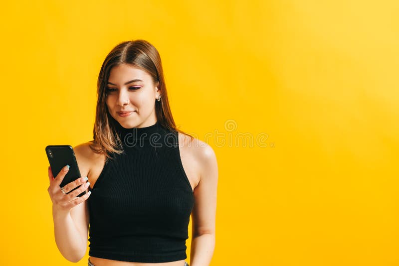 Attractive brunette young woman chatting with someone using mobile phone and smiling, hold phone in hands,  on yellow