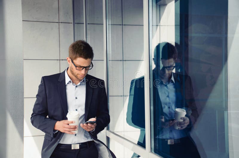 Attractive businessman with phone device and coffee in hands on