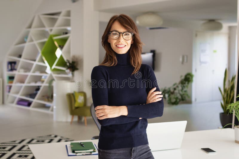 Attractive businesswoman standing at the office while looking at camera and smiling