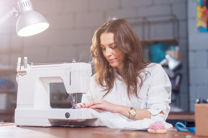 Attractive Caucasian seamstress working stitching with sewing machine at her workplace in studio loft interior royalty free stock photos