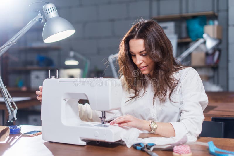 Attractive Caucasian seamstress working stitching with sewing machine at her workplace in studio loft interior stock photo