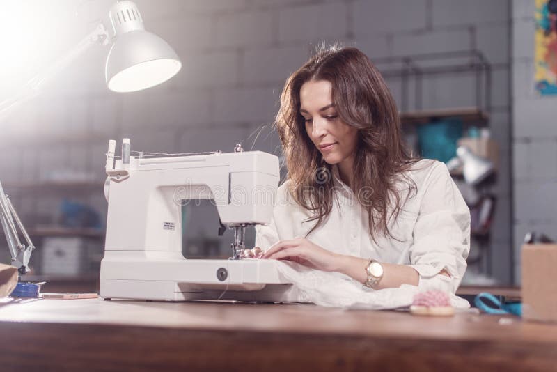 Attractive Caucasian seamstress working stitching with sewing machine at her workplace in studio loft interior stock images