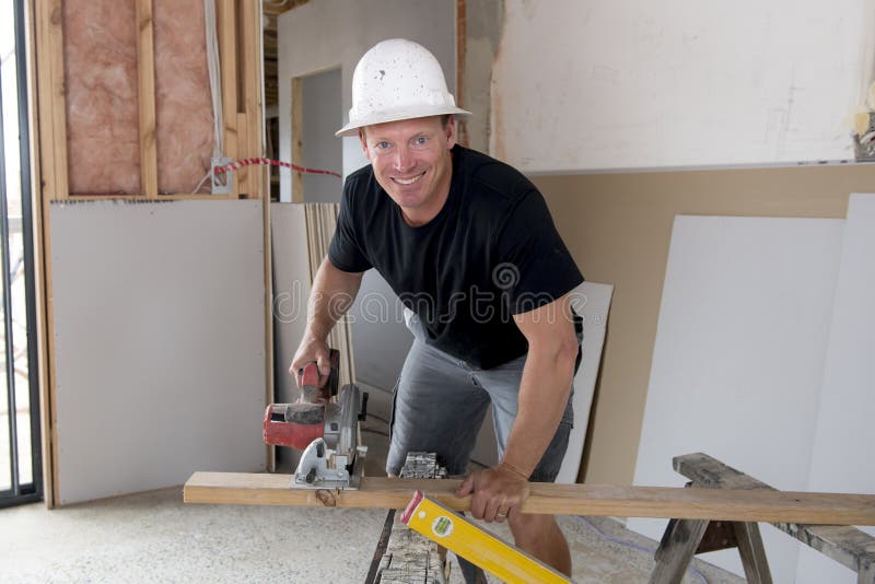 Attractive and confident constructor carpenter or builder man in protective helmet working cutting wood at industrial construction site in installation and renovation work industry. Attractive and confident constructor carpenter or builder man in protective helmet working cutting wood at industrial construction site in installation and renovation work industry