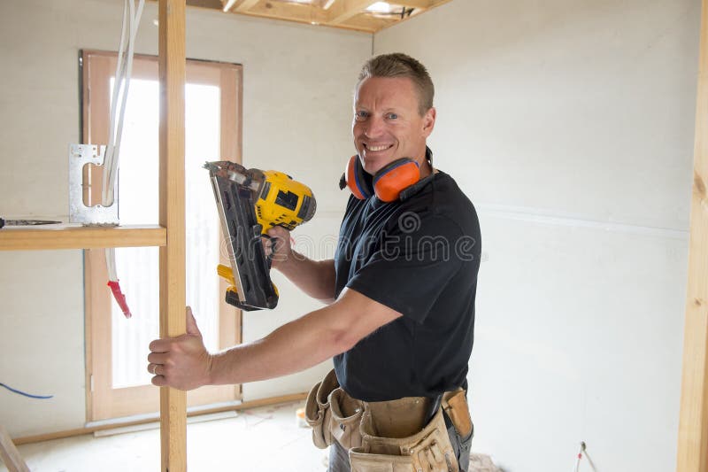 Attractive and confident constructor carpenter or builder man working wood with electric drill at industrial construction site in installation and renovation work industry