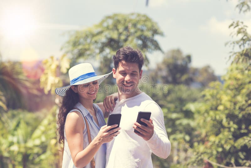 Attractive Couple Messaging Online Using Smart Phones Man And Woman Embracing Over Tropical Forest Landscape Smiling