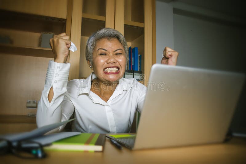 Attractive desperate and stressed middle aged Asian woman screaming gesturing overwhelmed and overwork working at office computer desk feeling exploited and upset in work stress