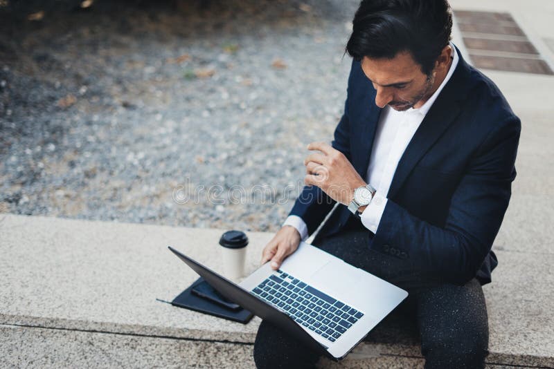 Attractive elegant businessman using contemporary notebook and smartphone sitting outside.Blurred background. Horizontal royalty free stock photos Attractive elegant businessman using contemporary notebook and smartphone sitting outside.Blurred background. Horizontal royalty free stock photos