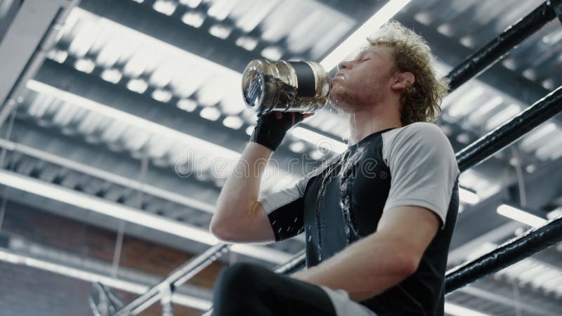 Attractive fighter drinking water in fitness center. Sportsman quenching thirst