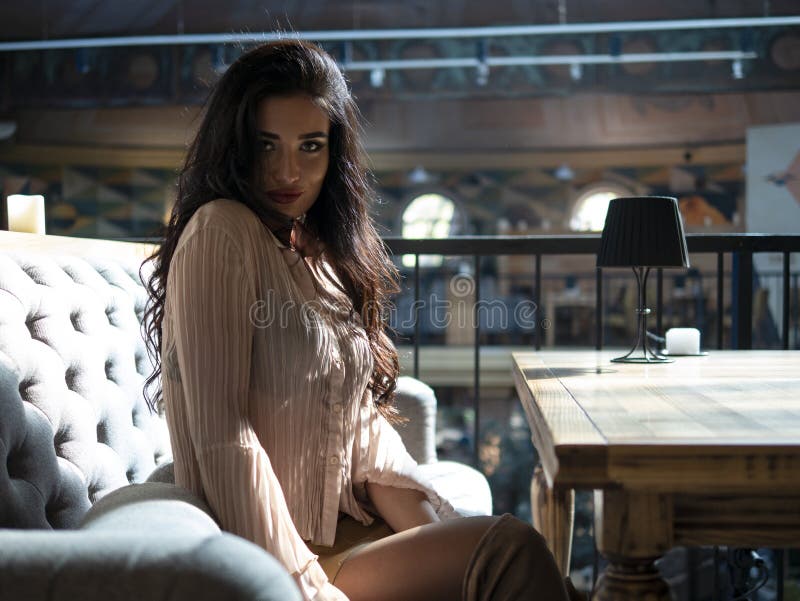 Attractive girl with curly hair and long legs in a short skirt is sitting on the sofa at the table stock photos Attractive girl with curly hair and long legs in a short skirt is sitting on the sofa at the table stock photos