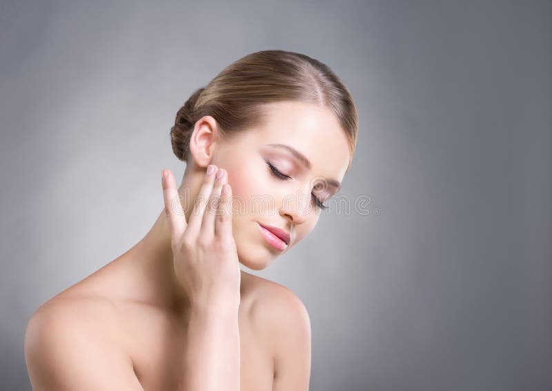 Attractive girl touching her smooth skin over cheeks on grey background royalty free stock photography Attractive girl touching her smooth skin over cheeks on grey background royalty free stock photography