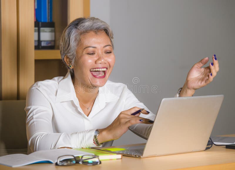 Attractive and happy successful middle aged business Asian woman working at laptop computer desk smiling confident in entrepreneur stock image Attractive and happy successful middle aged business Asian woman working at laptop computer desk smiling confident in entrepreneur stock image