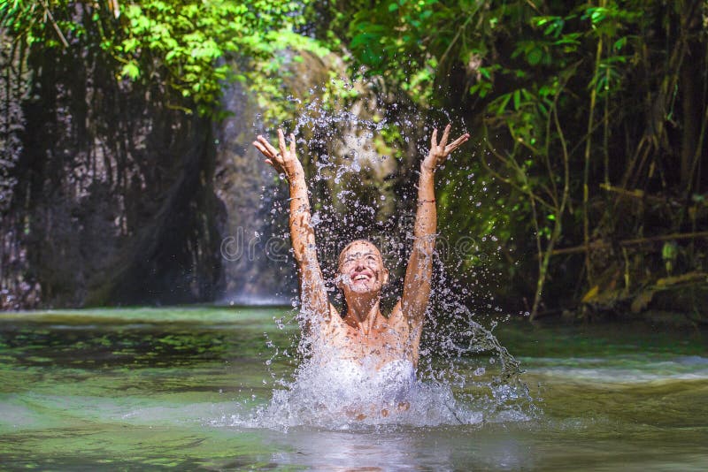 Attractive happy white tourist woman enjoying playing with water and splash at tropical exotic waterfall lagoon holidays travel co