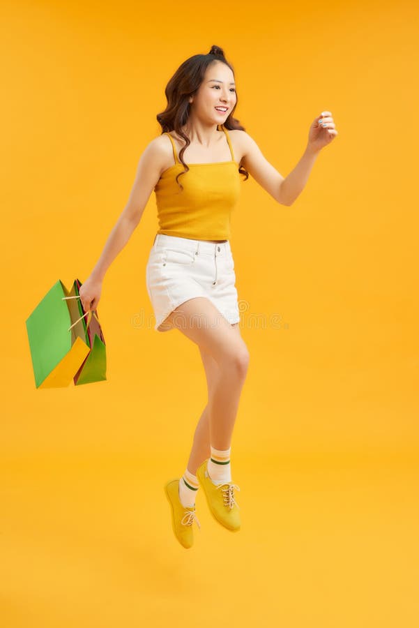 Attractive happy woman jumping running holding shopping bags over orange background. Summer concept